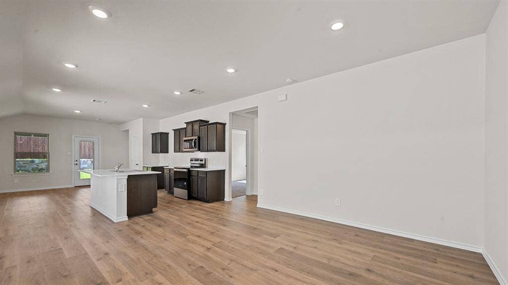Wood-finish flooring, recessed lighting, vaulted ceiling, kitchen island with sink, and dark cabinetry