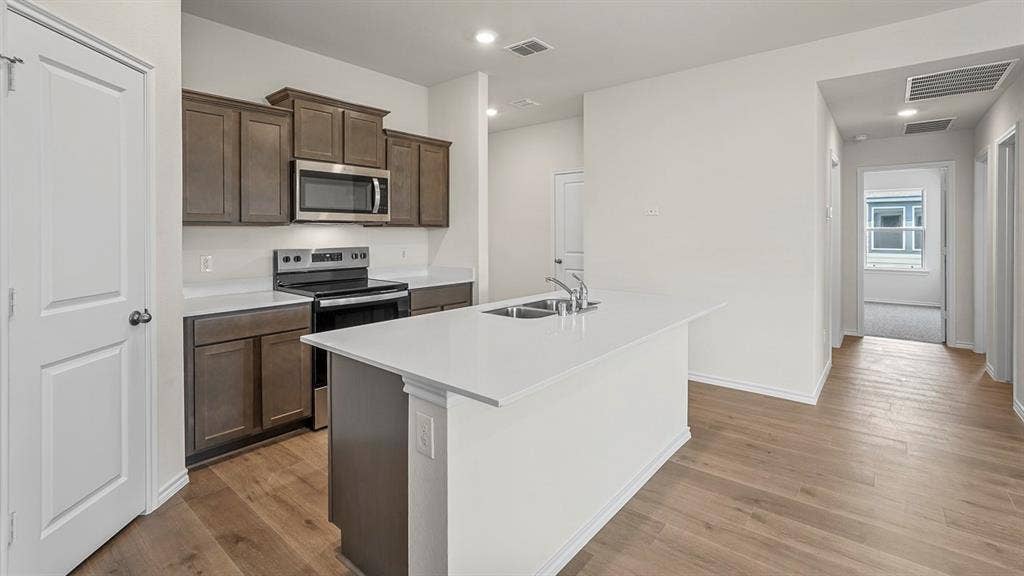 Kitchen featuring dark wood-finish cabinetry, quartz countertops, a central island with a double-basin sink, stainless steel appliances, and wood-finish flooring