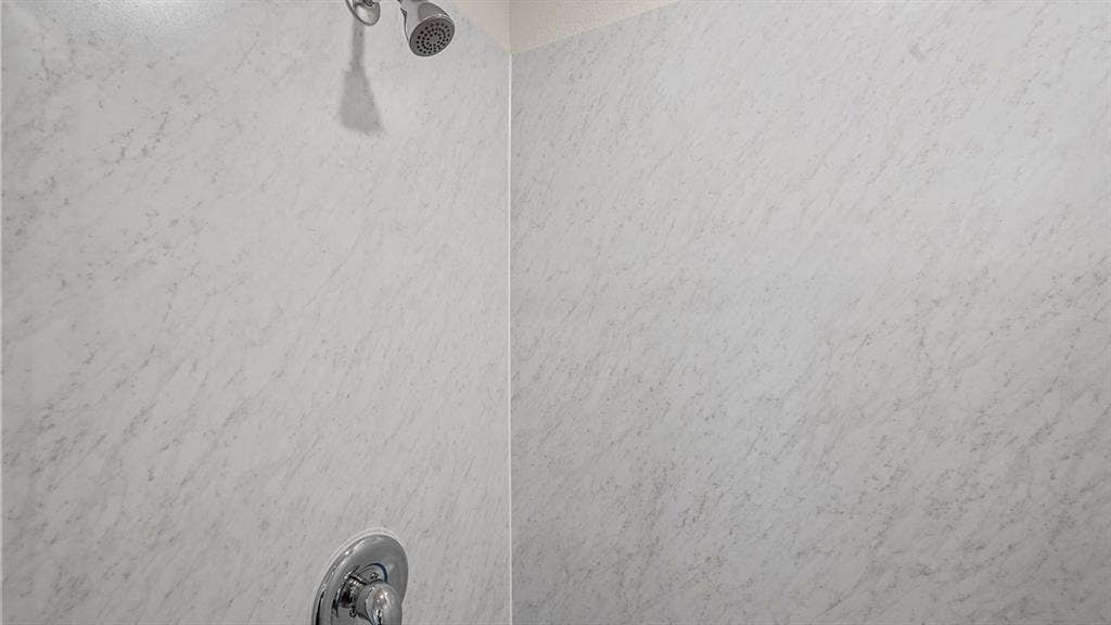 Shower enclosure featuring stone-patterned surround panels, polished chrome fixture, and circular control handle
