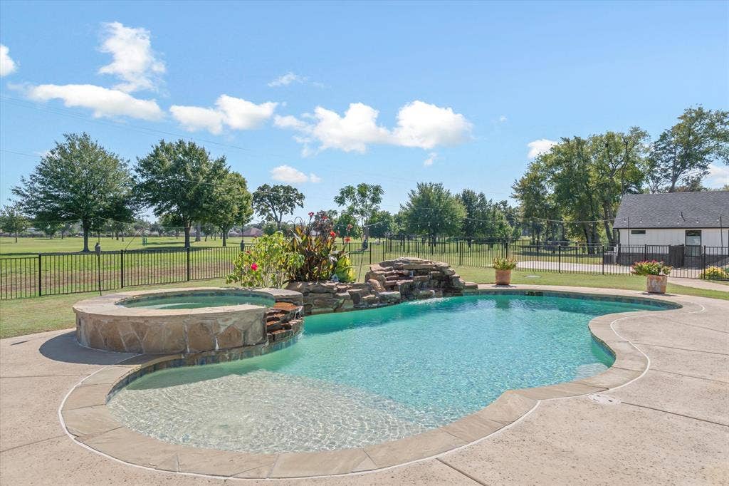 203 Splitrail Drive, Mabank, TX 75143 In-ground pool featuring a stone waterfall, integrated raised spa, concrete decking, and metal perimeter fencing