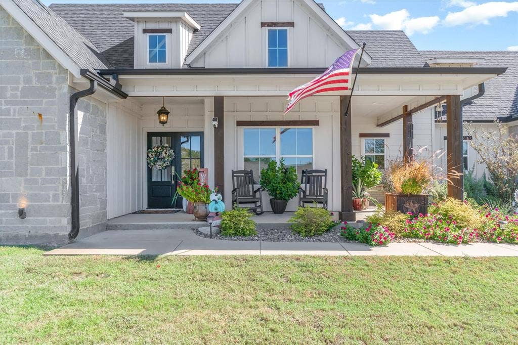 203 Splitrail Drive, Mabank, TX 75143 Modern farmhouse exterior featuring vertical board-and-batten siding, natural stone veneer accents, a covered front porch with timber posts, and a dark-framed glass paneled front door