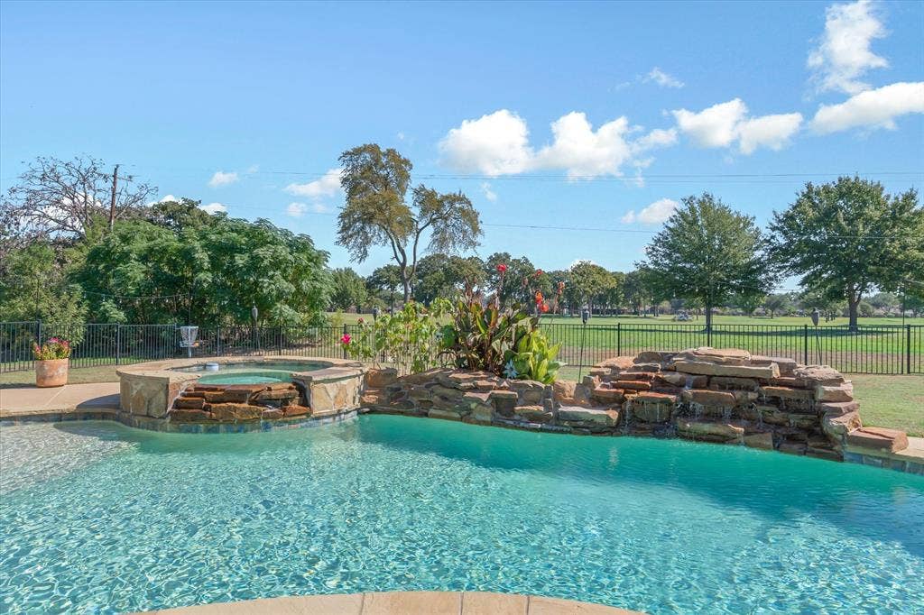 203 Splitrail Drive, Mabank, TX 75143 In-ground swimming pool featuring a stacked stone waterfall, integrated spill-over spa, and perimeter wrought-iron fencing