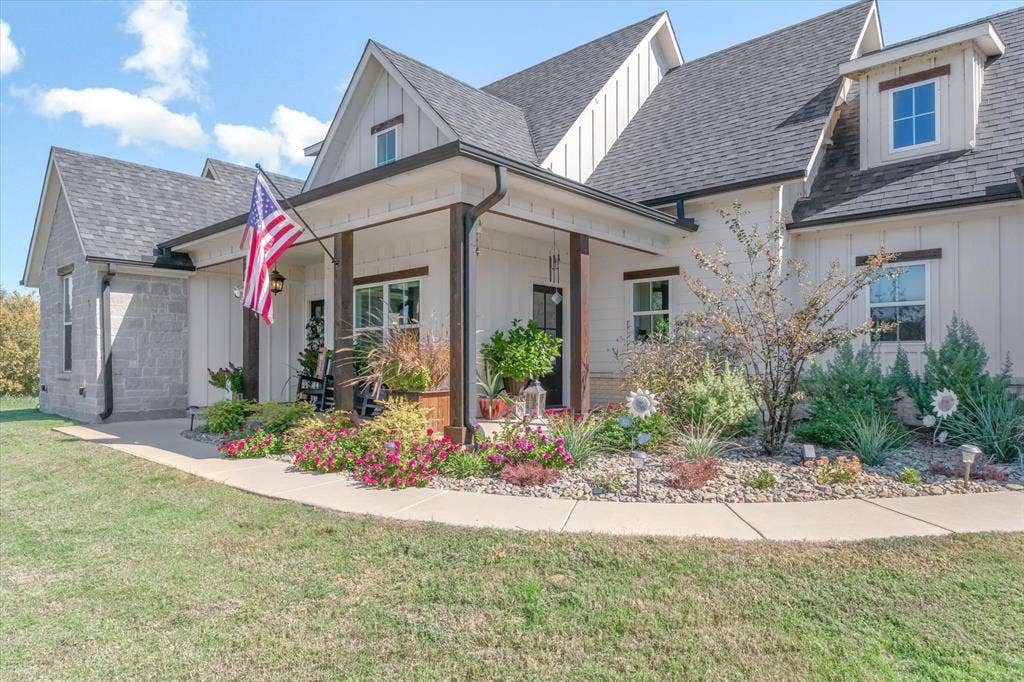 203 Splitrail Drive, Mabank, TX 75143 Modern farmhouse exterior featuring vertical board-and-batten siding, stone masonry accents, a covered front porch with timber-frame support columns, and multi-gabled rooflines
