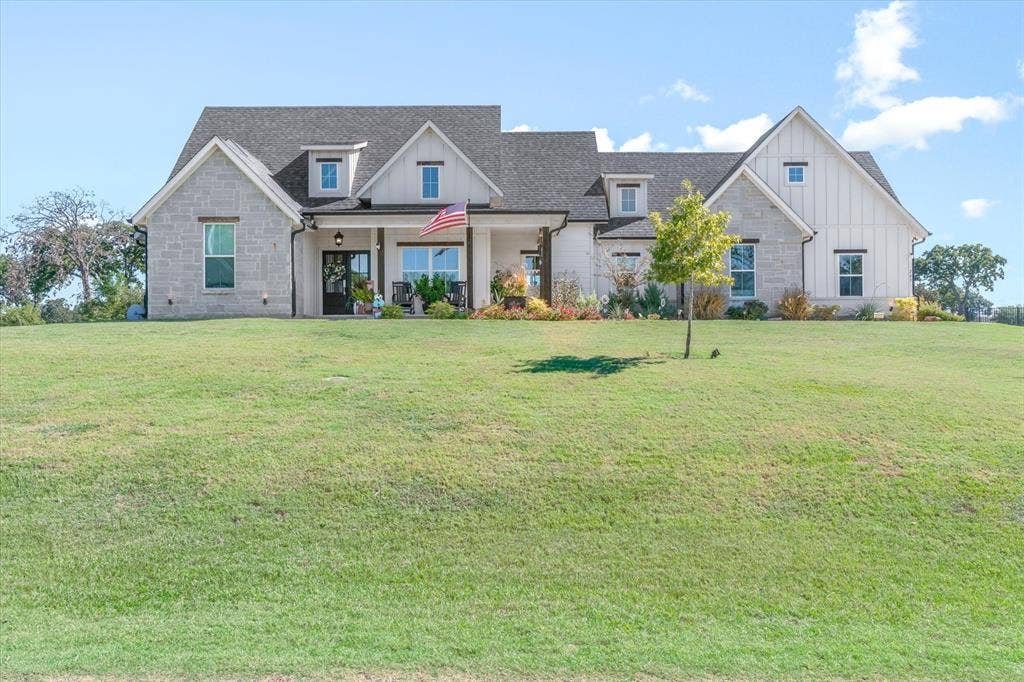 203 Splitrail Drive, Mabank, TX 75143 Multi-gabled exterior featuring light-toned stone masonry, vertical board-and-batten siding, a covered front porch with timber support columns, and expansive front lawn
