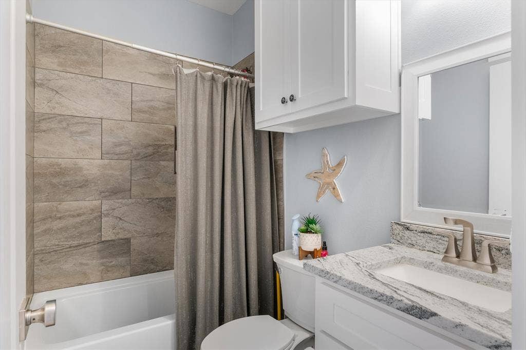 203 Splitrail Drive, Mabank, TX 75143 Bathroom featuring a vanity with a light-toned stone countertop, white cabinetry, a framed mirror, and a tub surround finished in large-format neutral-toned tiles