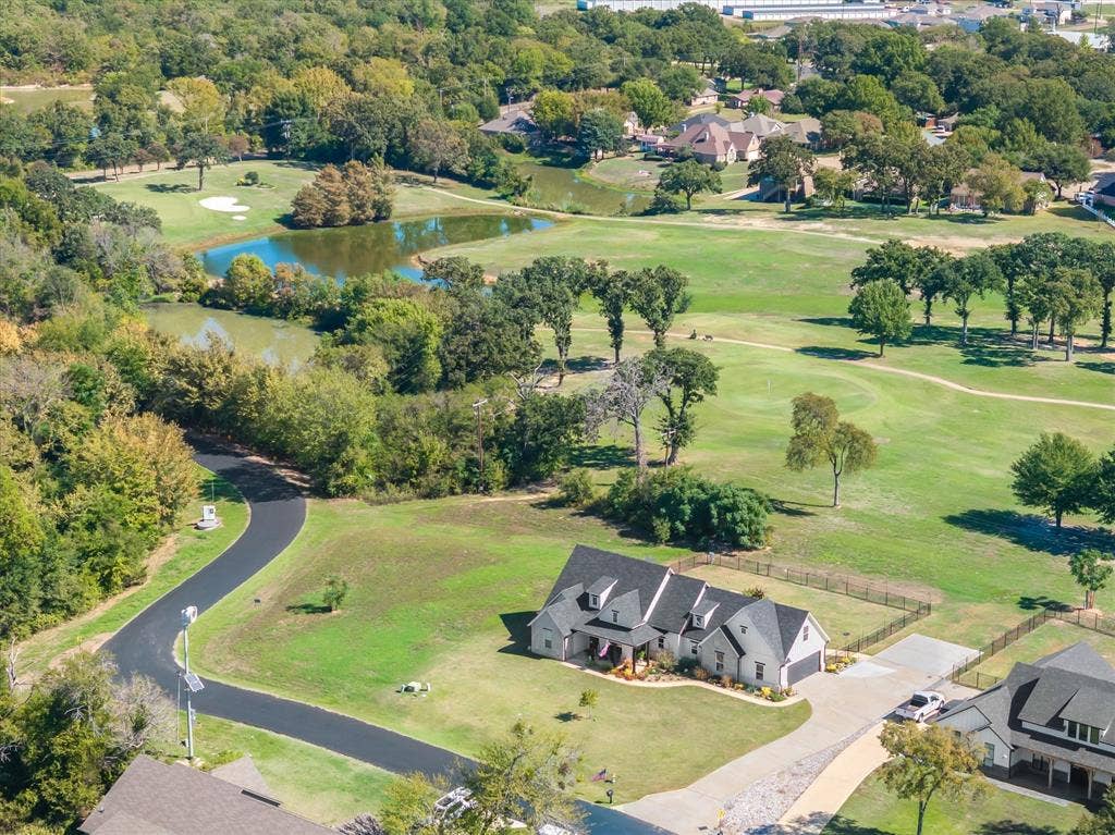 203 Splitrail Drive, Mabank, TX 75143 Aerial perspective featuring a multi-gabled residence with a paved driveway, expansive lawn, and direct exposure to a golf course landscape with water features and mature trees