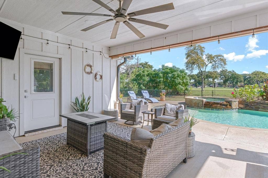 203 Splitrail Drive, Mabank, TX 75143 Covered patio with board-and-batten siding and a ceiling fan, featuring a swimming pool with a stone-accented water feature