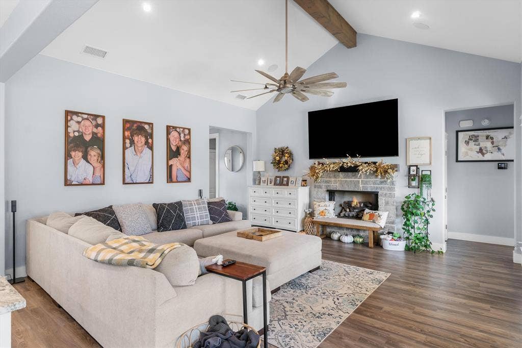 203 Splitrail Drive, Mabank, TX 75143 Vaulted ceilings with exposed wooden beam, stacked-stone fireplace, wood-finish flooring, and multi-blade ceiling fan