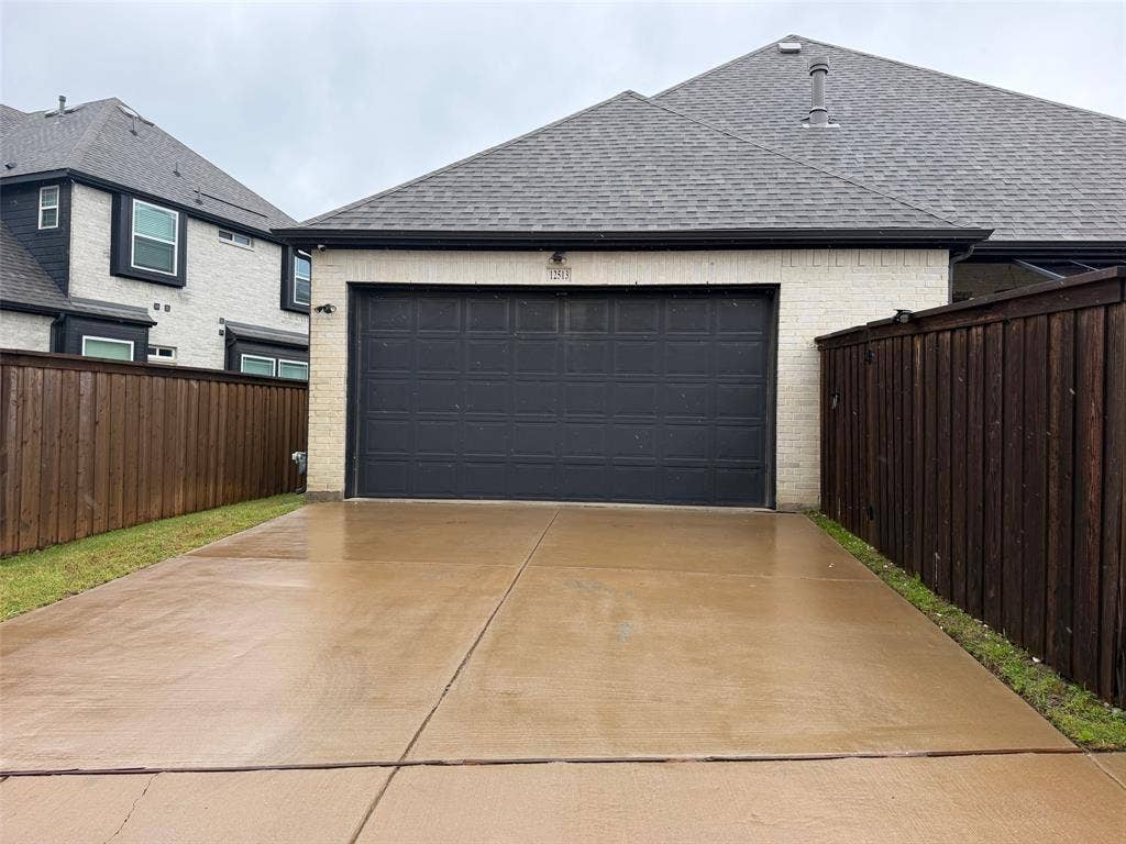 Light-colored masonry exterior featuring a dark-toned paneled garage door, composition shingle roof, and wooden privacy fencing