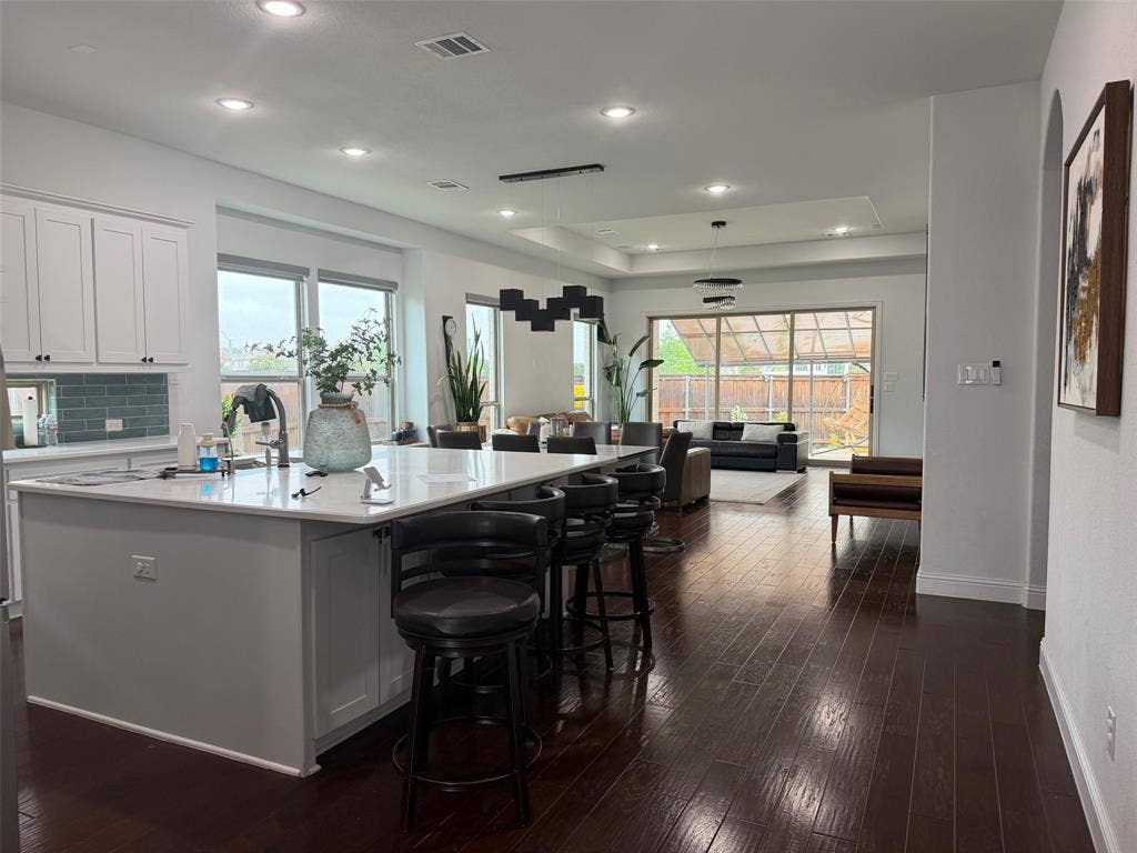 Kitchen featuring a spacious island with quartz countertops, custom white cabinetry, blue tile backsplash, wood-finish flooring, and recessed ceiling lighting