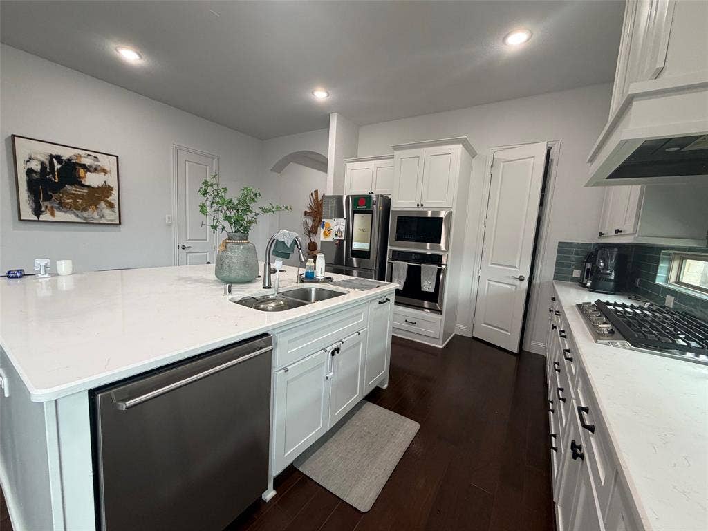 Kitchen featuring white shaker-style cabinetry, a large center island with a stone-surface countertop, stainless steel built-in double ovens, a gas cooktop, and dark wood-finish flooring