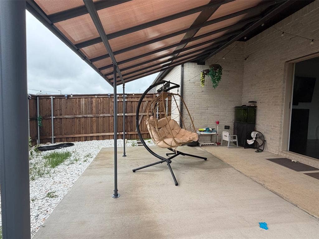 Covered concrete patio featuring a dark metal frame structure, masonry exterior wall, and wood privacy fencing