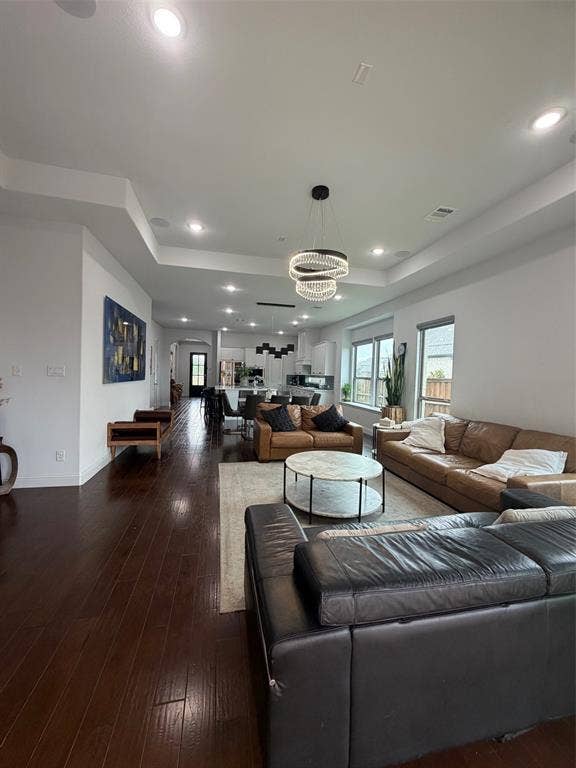 Open-concept living space featuring wood-finish flooring, tray ceilings, recessed lighting, and a tiered crystal chandelier