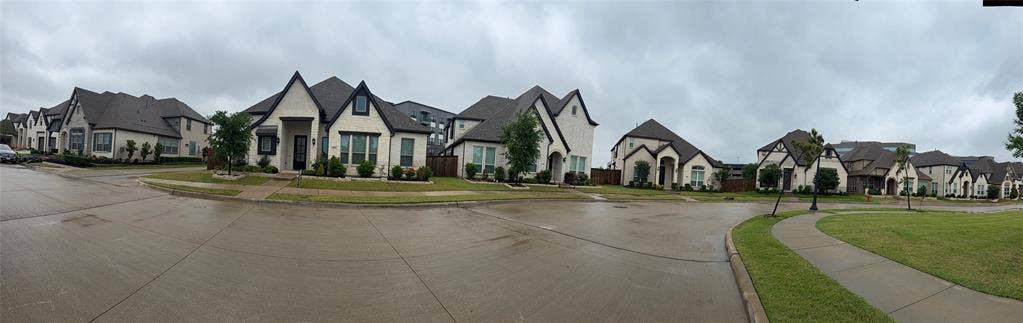 Street-level panoramic view of residential exteriors featuring multi-gabled rooflines, light-toned masonry facades, dark-trimmed window frames, and concrete driveways