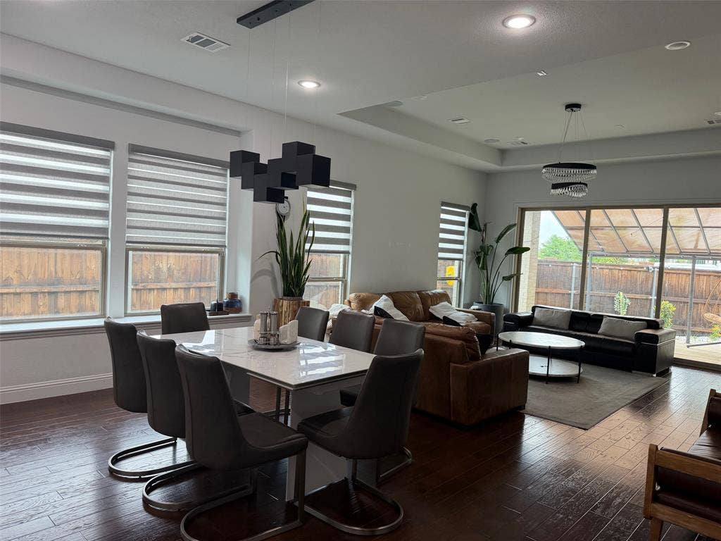 Open-concept interior featuring wood-finish flooring, tray ceilings, recessed lighting, geometric pendant fixtures, and large sliding glass doors
