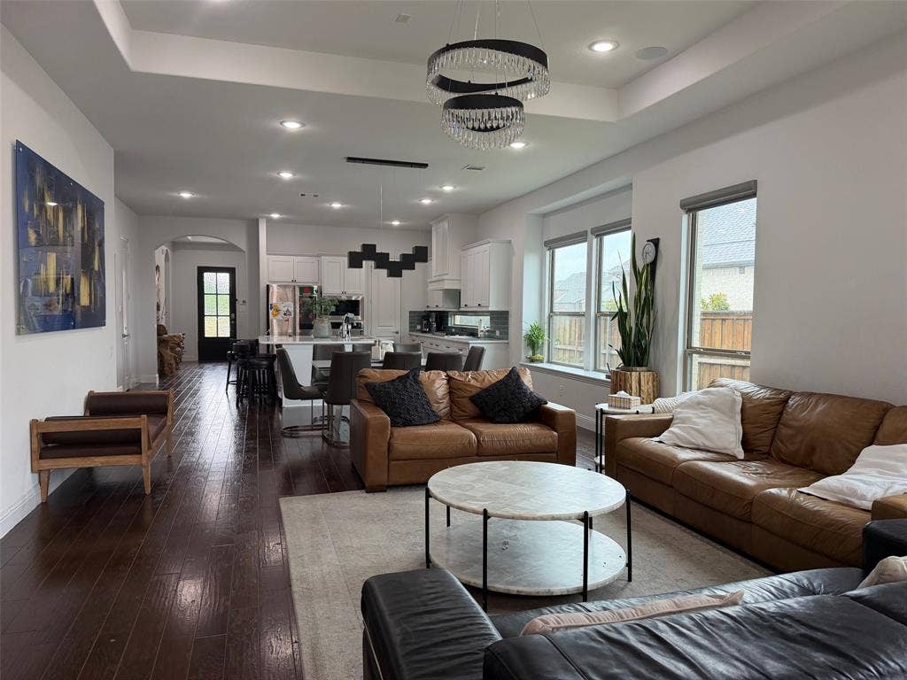 Open-concept living space featuring wood-finish flooring, tray ceilings, recessed lighting, and a tiered crystal chandelier