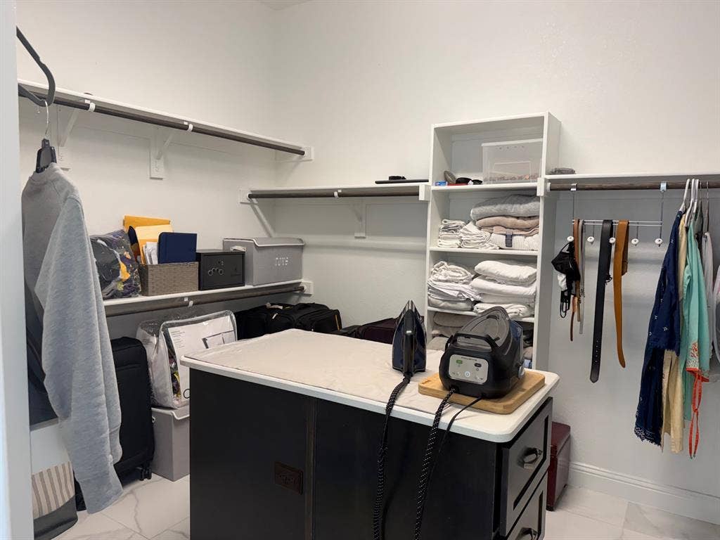 Walk-in closet featuring white built-in shelving, dual-tier wall-mounted rods, and a center island with a solid surface countertop and integrated drawer storage