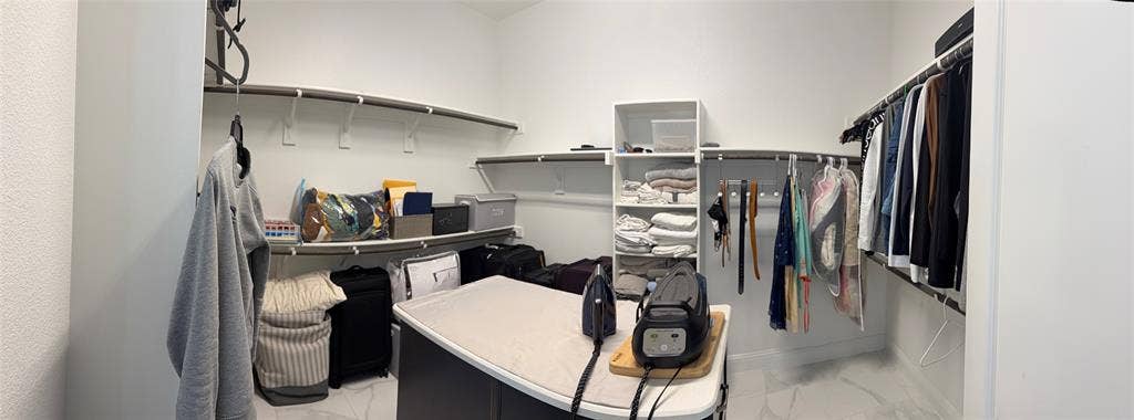 Walk-in closet featuring extensive built-in shelving, white tiered organization tower, multi-level clothing rods, and light-toned stone-patterned flooring
