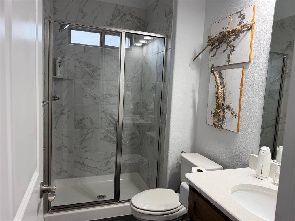 Walk-in shower with stone-finish tile surround and glass enclosure, vanity with integrated basin and light-toned countertop, and recessed ceiling lighting