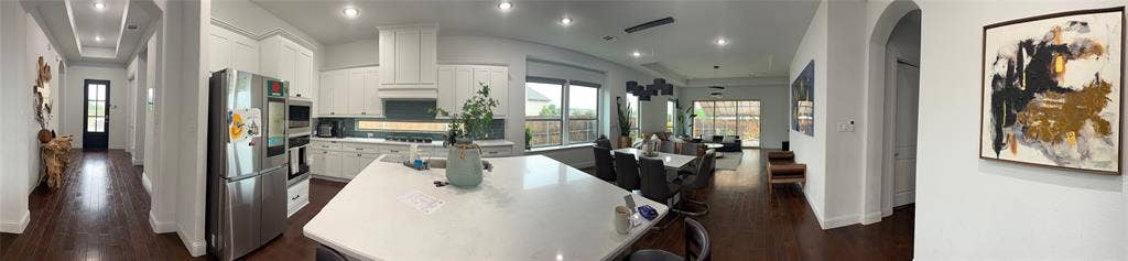 Kitchen featuring a large stone-surface island, white cabinetry, integrated stainless steel appliances, recessed lighting, and wood-finish flooring
