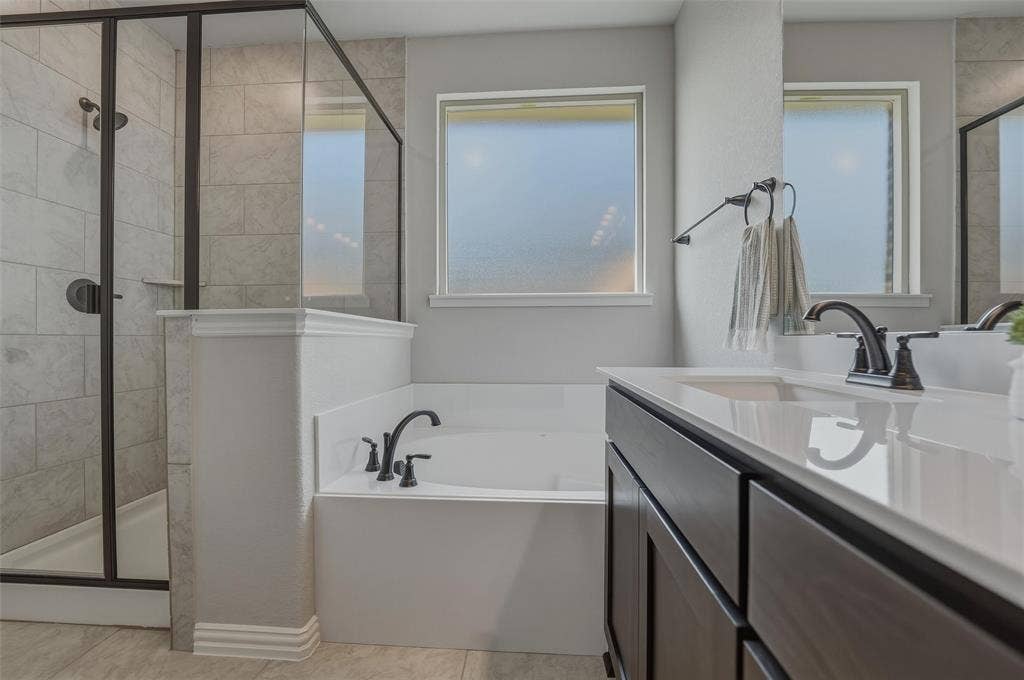 Built-in soaking tub, separate glass-enclosed shower with tile surround, dark wood-finish vanity with an integrated sink, and dual frosted windows