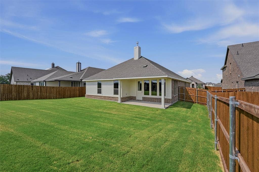 Expansive backyard featuring a manicured lawn, full perimeter fencing, and a covered patio with brick and siding exterior