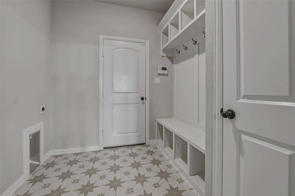 Mudroom featuring patterned floor tiles, built-in bench with storage cubbies, and overhead shelving with hooks