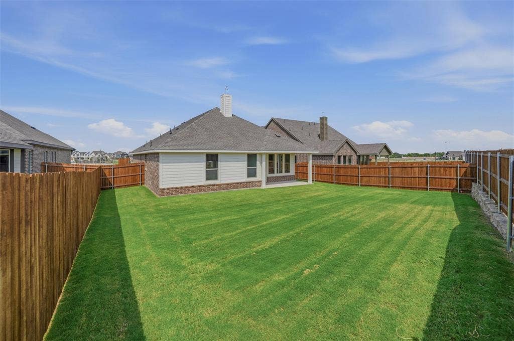 Expansive lawn with a full privacy fence, covered patio, and brick and siding exterior