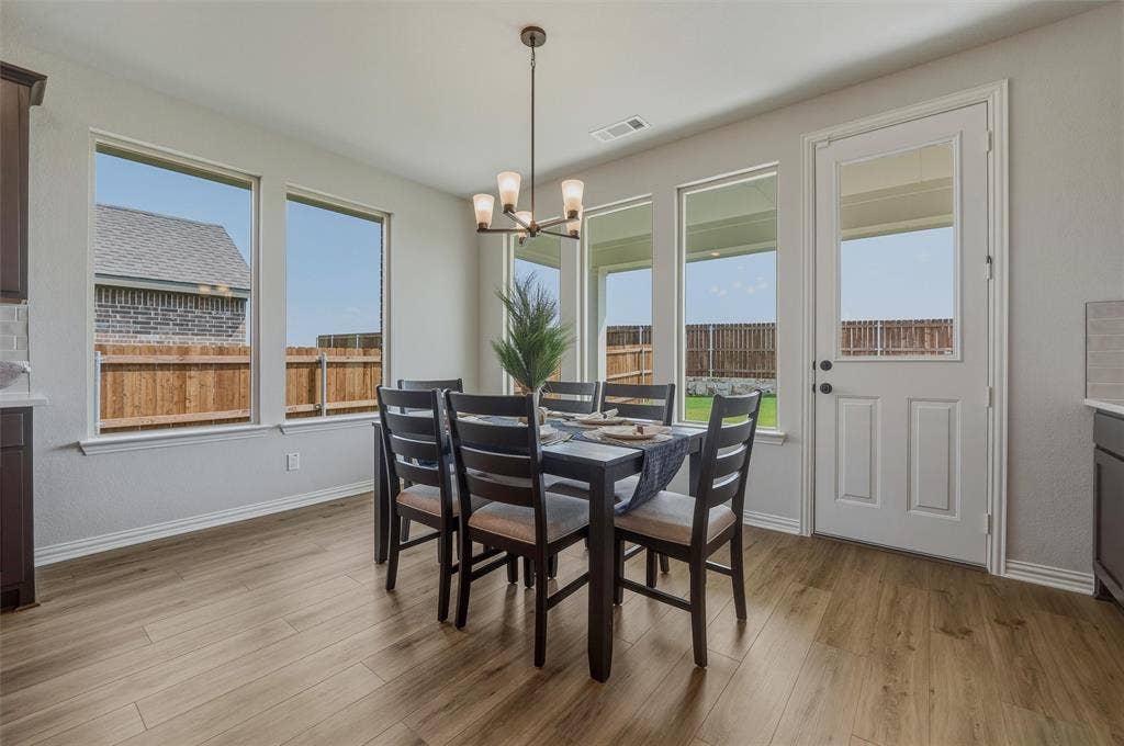 Wood-finish flooring, multiple large windows, a built-in ceiling light fixture, and a white door with an upper glass panel