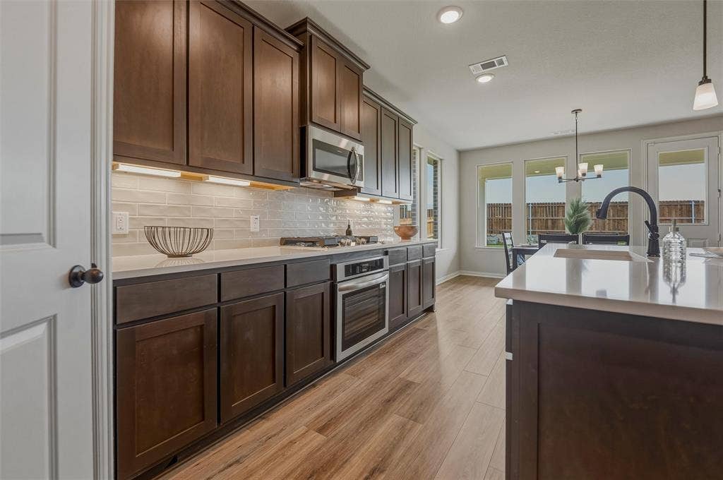 Dark wood-finish cabinetry, light-toned countertops, stainless steel appliances, and wood-finish flooring