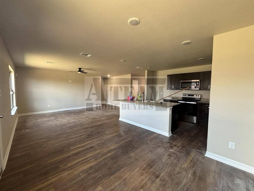 Open-concept space featuring wood-finish flooring, recessed lighting, dark cabinetry, stone-surface countertops, and a kitchen island