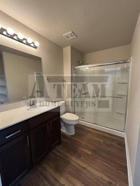Dark wood-finish cabinetry, light-toned countertop with an integrated sink, polished hardware, wood-finish flooring, and a glass-enclosed shower stall