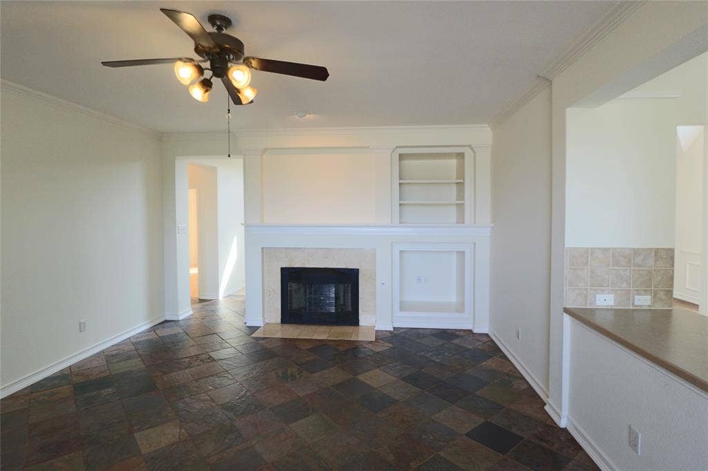 Living room with built in cabinets, fire place and ceiling fan, open to the kitchen.