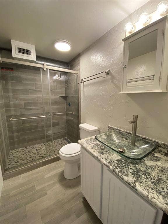 Full bath with a textured wall, vanity, a shower stall, and wood finish floors