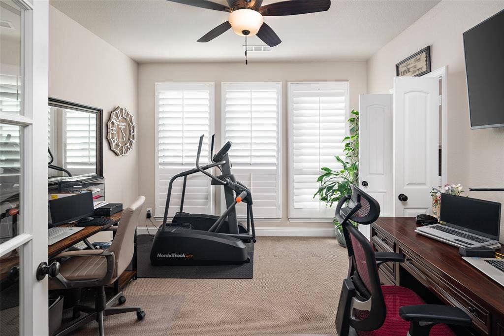 Room featuring three windows with plantation shutters, ceiling fan with light kit, carpeted flooring, and glass-paneled interior French door