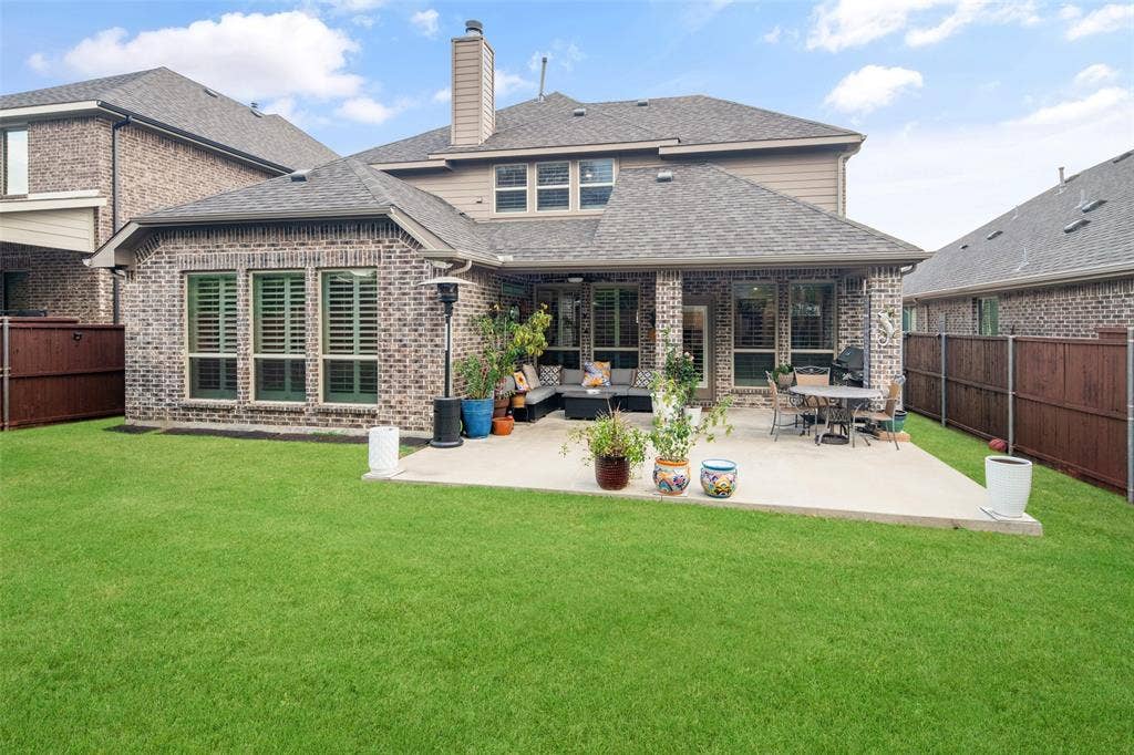 Rear exterior featuring a brick facade, covered concrete patio, chimney, and enclosed backyard with wood fencing
