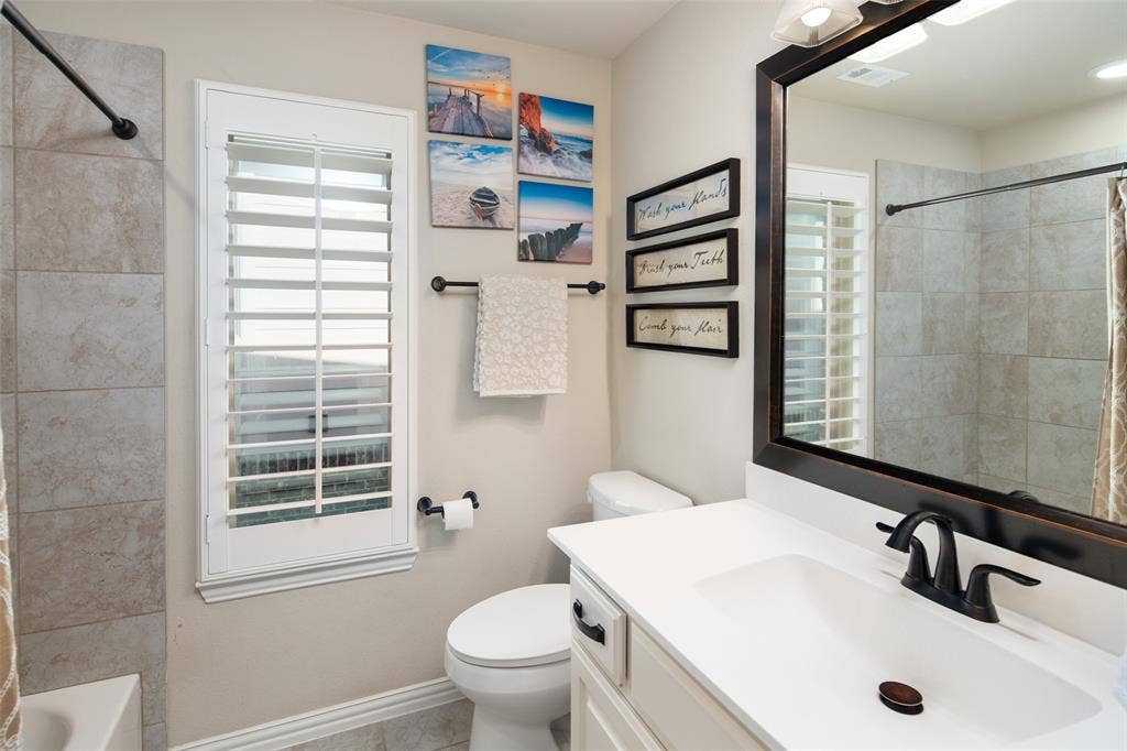 Bathroom featuring a vanity with a solid-surface countertop, rectangular undermount sink, and matte black hardware, accompanied by plantation shutters and wall-surround tile