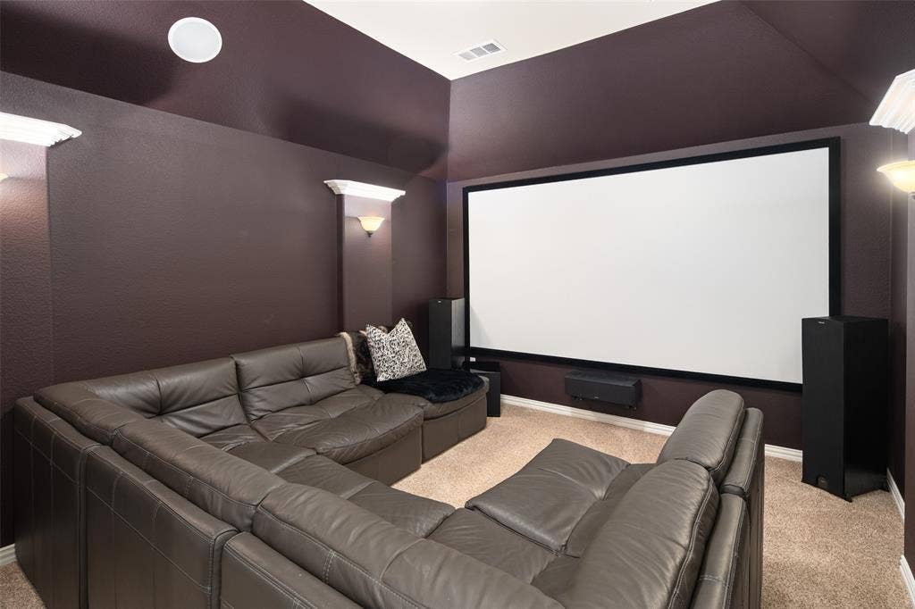 Media room featuring high vaulted ceilings, wall-mounted screen, integrated sconce lighting, and carpeting