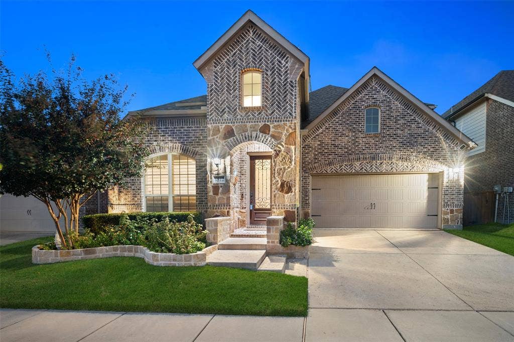 Multi-gabled brick and stone exterior featuring a herringbone-patterned gable peak, arched masonry entryway, leaded glass front door, and a concrete driveway