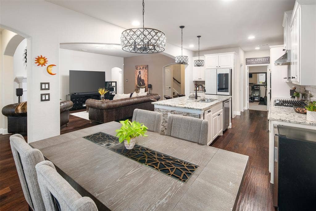 Kitchen featuring white shaker-style cabinetry, stone-finish countertops, stainless steel appliances, a center island with a dual-basin sink, and dark wood-finish flooring