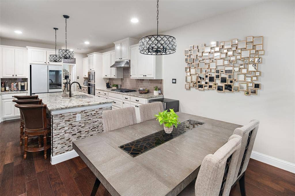 Kitchen featuring white cabinetry, stone countertops, a center island with stone tile detailing, recessed lighting, and metal pendant fixtures, all complemented by wood-finish flooring