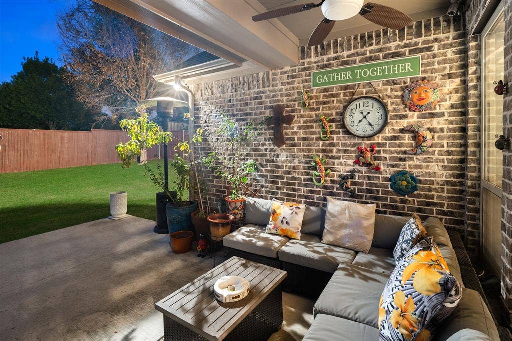 Covered patio featuring a brick accent wall, concrete flooring, and an integrated ceiling fan
