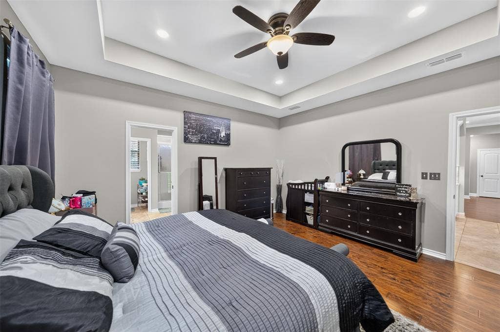 Tray ceiling featuring recessed lighting and a central ceiling fan with an integrated light fixture, complemented by wood-finish flooring