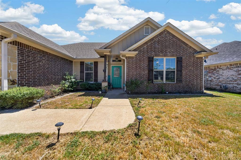 Single-story brick exterior featuring a gable roof, decorative shutters, concrete walkway, and built-in landscape lighting
