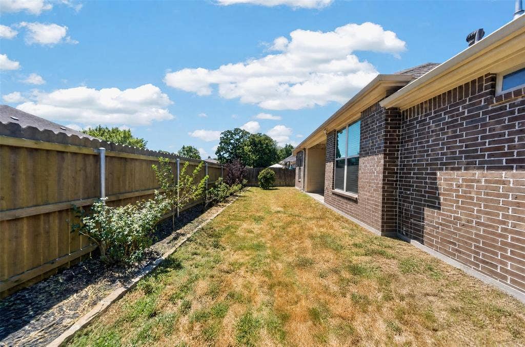 Rear exterior featuring brick masonry siding, a wooden privacy fence, and a designated planting strip along the perimeter