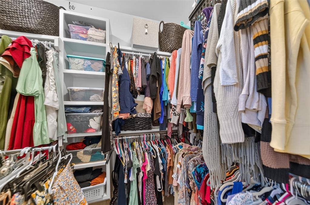 Walk-in closet featuring white built-in shelving and multi-level hanging rods