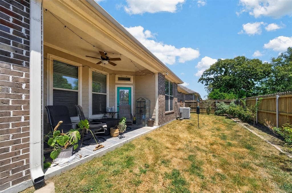 Covered patio featuring a concrete slab, brick exterior cladding, a ceiling-mounted fan, and a wood-slatted privacy fence