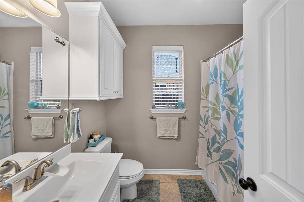 Bathroom featuring a vanity with a countertop sink, brushed metal faucet, upper cabinetry, and tile flooring