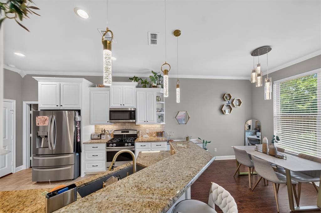 Kitchen featuring white cabinetry, stone countertops, stainless steel appliances, tiered pendant lighting, and wood-finish flooring