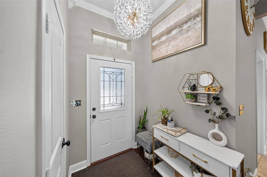 Entryway featuring a decorative glass-panel door, a transom window, crown molding, and a spherical crystal pendant light fixture